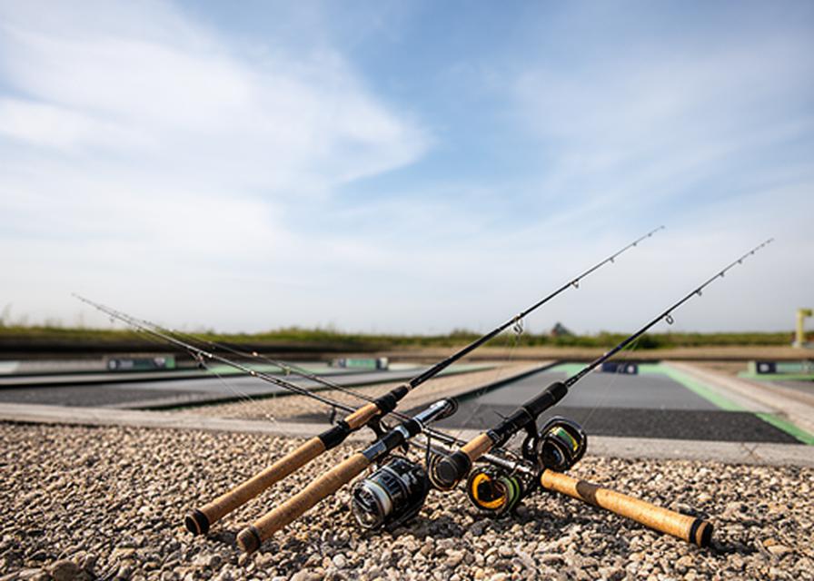 Fly rods and reels arranged beside a casting practice lane with open sky and smooth gravel underfoot